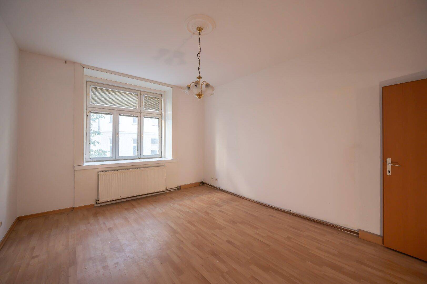 Leeres Wohnzimmer mit Parkettboden, Fenster und Deckenleuchte, bereit zur Renovierung.