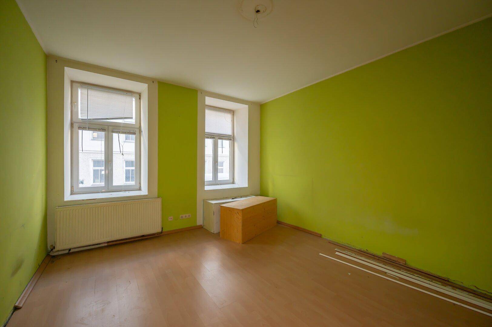 Leeres Zimmer mit auffälligen grünen Wänden und Holzboden, bereit zur Renovierung.