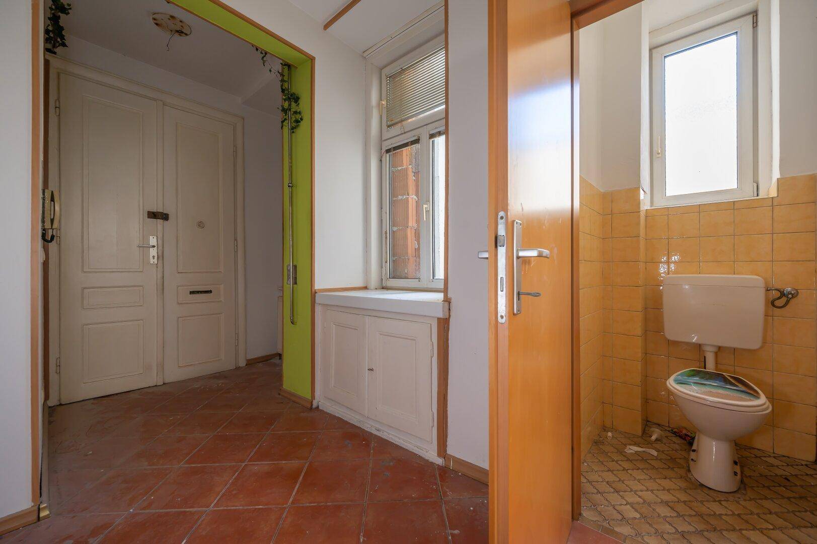 Eingangsbereich mit Terrakottafliesen und einer separaten Toilette in einem kleinen Raum.