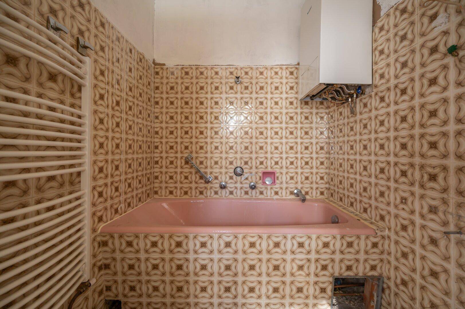 Badezimmer mit rosa Badewanne und gemusterten Fliesen, benötigt eine Modernisierung.