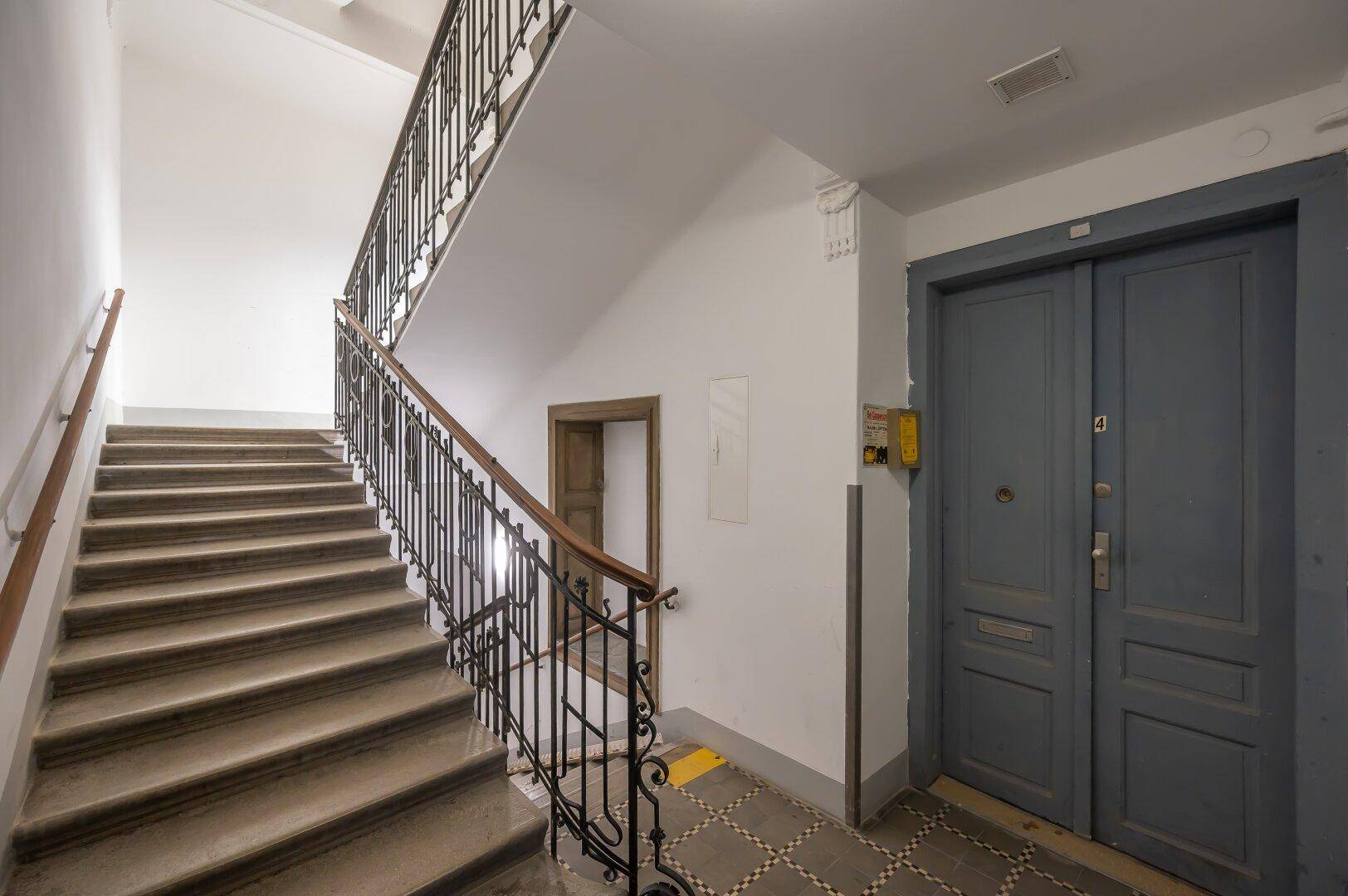 Treppenhaus mit historischem Geländer und Aufzug in einem Altbaugebäude.