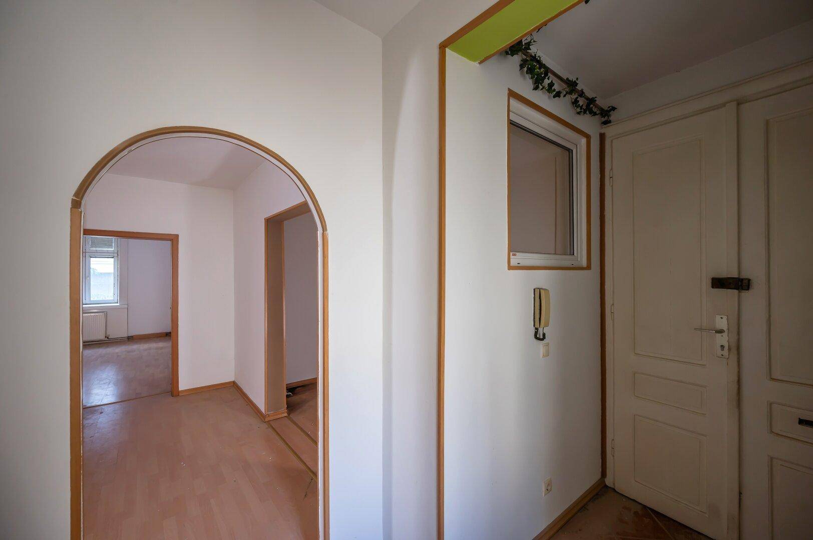 Heller Flur mit Holzboden und Rundbogen, verbindet die verschiedenen Räume der Wohnung.