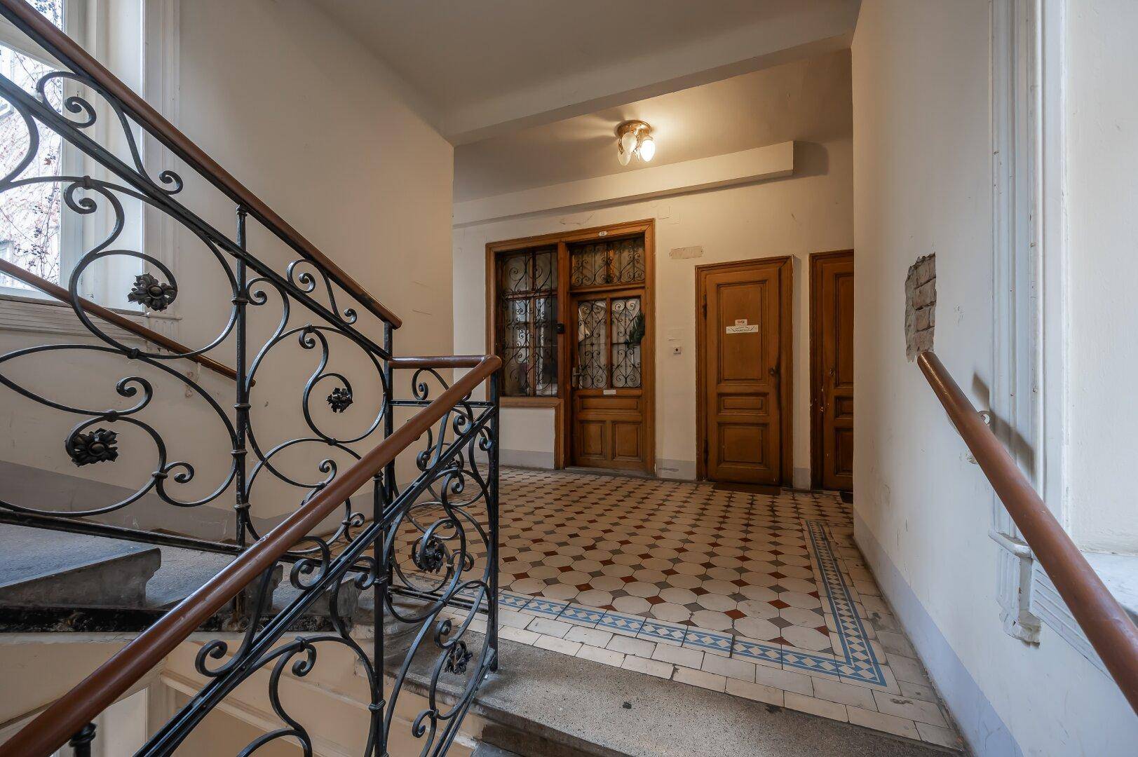 Historisches Treppenhaus mit schmiedeeisernem Geländer und gemustertem Fliesenboden.