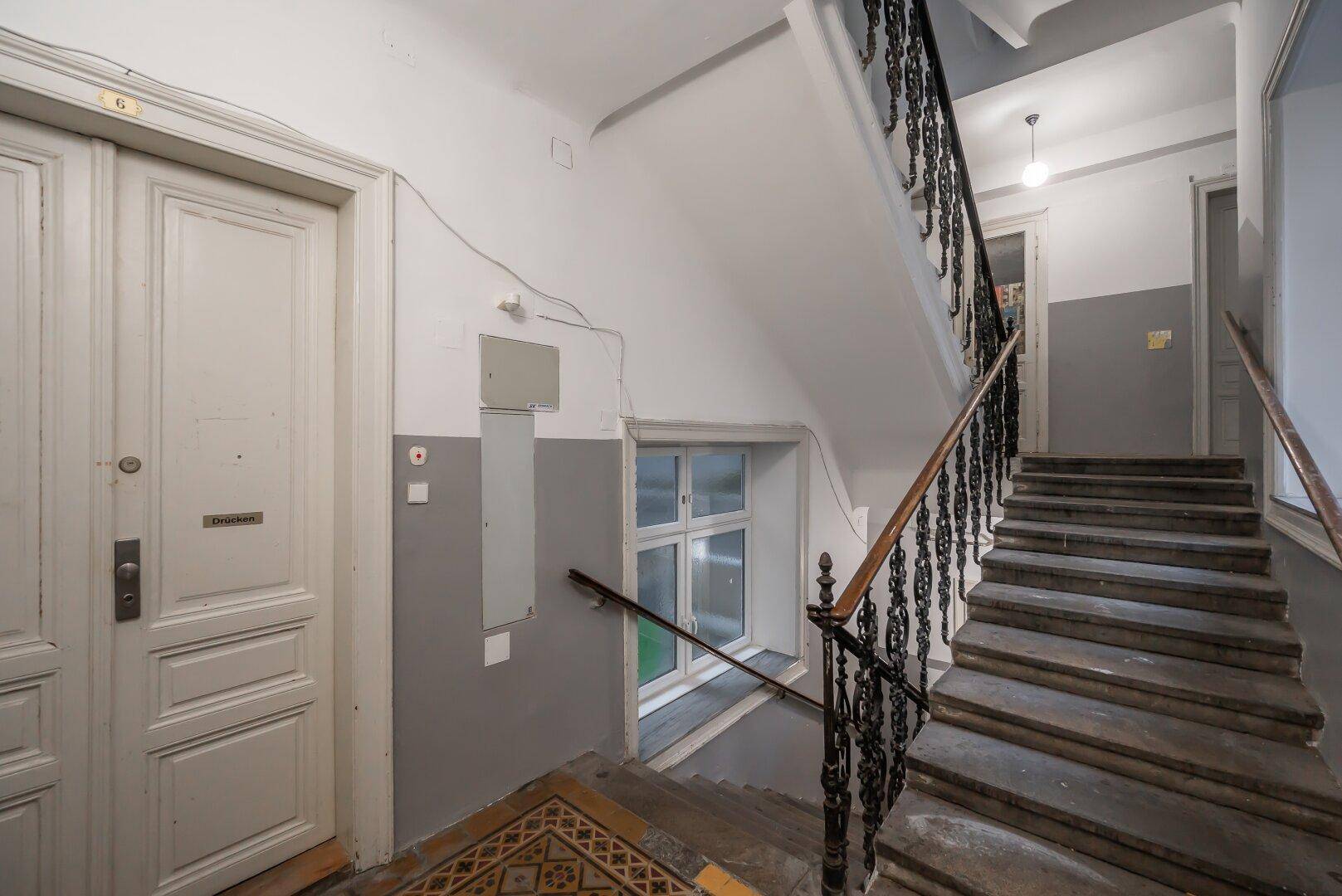 Treppenhaus eines Altbaus mit Holzstufen, schmiedeeisernem Geländer und weiß gestrichenen Türen.