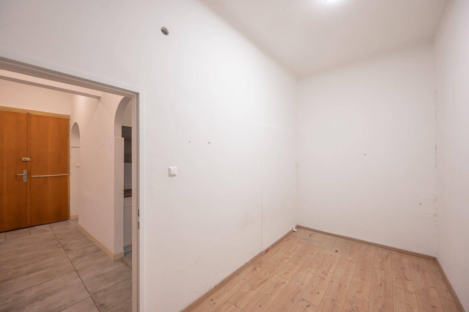 Helles, leeres Zimmer mit Holzboden und Blick in einen gefliesten Flur.