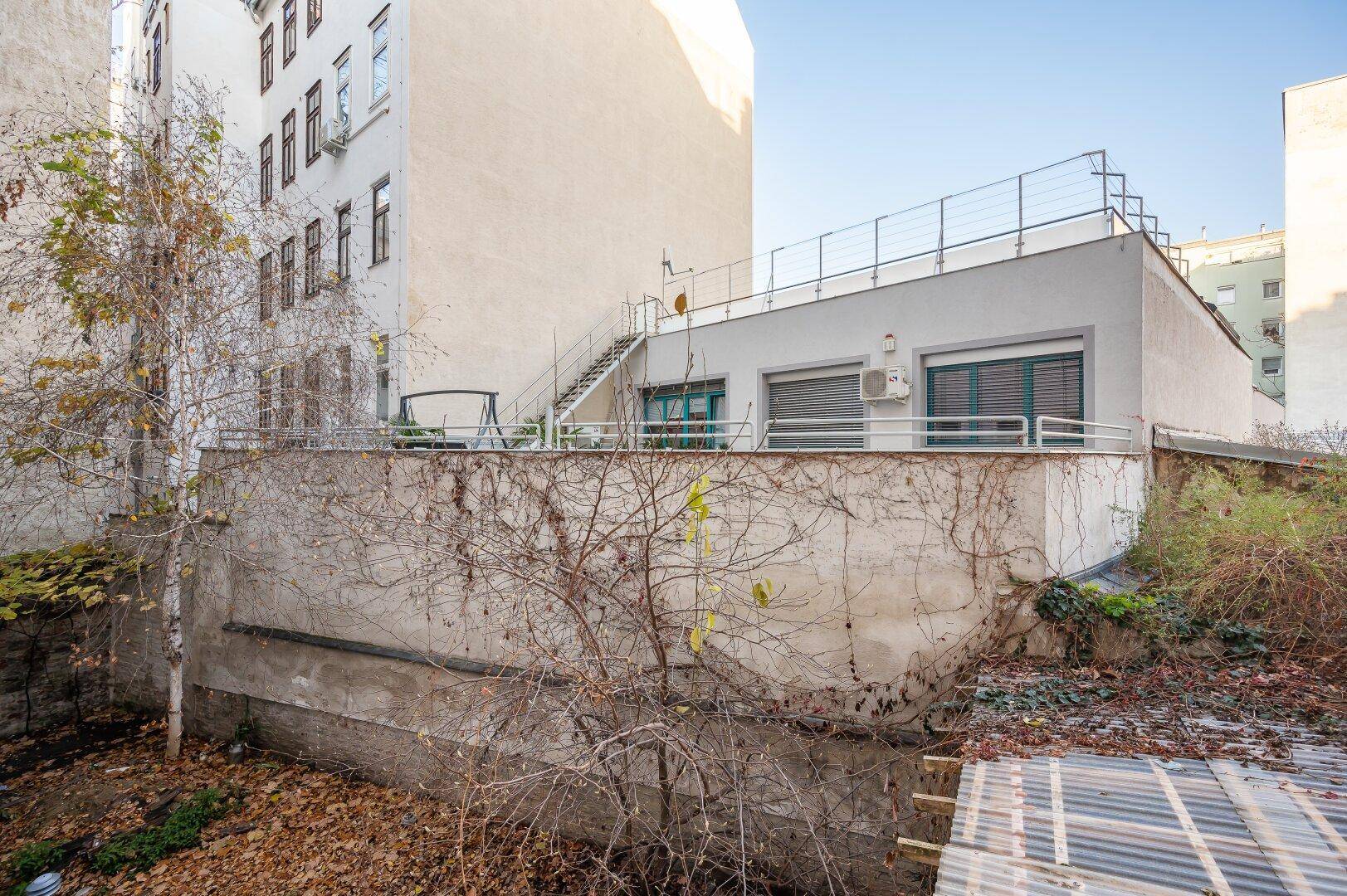 Hinterhofansicht eines Gebäudes mit einer Terrasse und Treppe zu einem oberen Bereich.