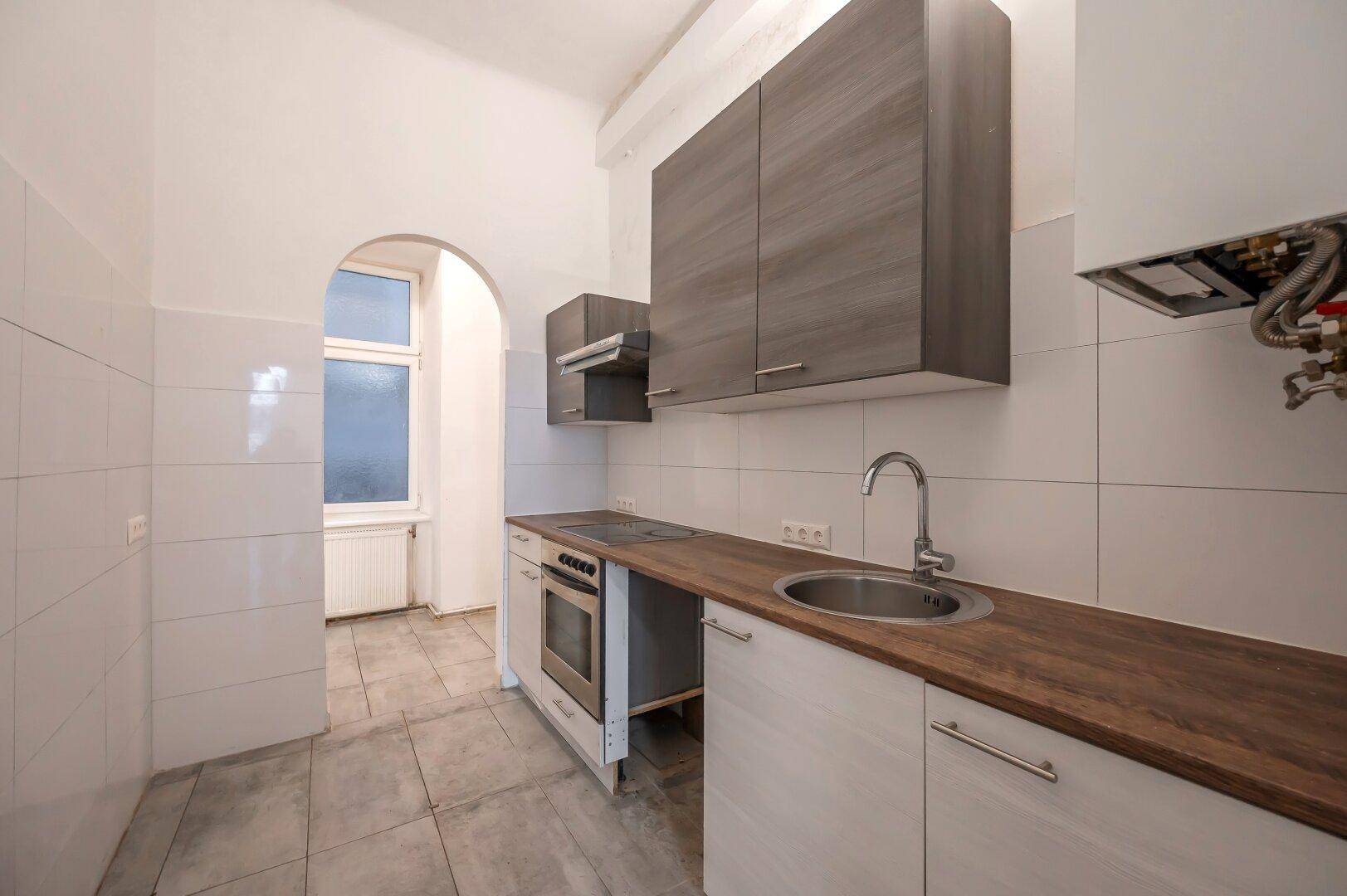 Moderne Küchenzeile mit weißen Fliesen, Holztheke und grauen Oberschränken.