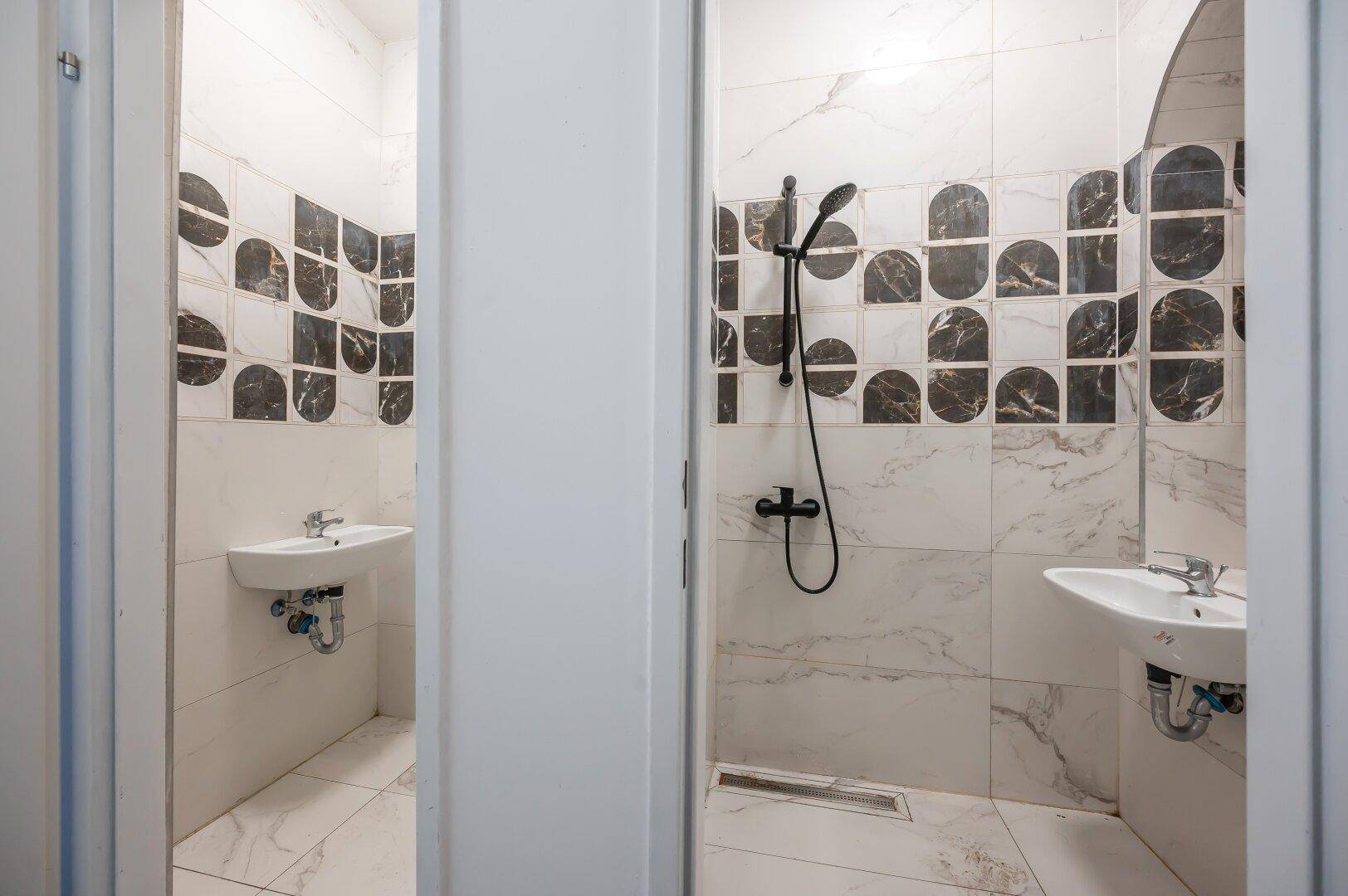 Helles Badezimmer mit zwei Waschbecken, begehbarer Dusche und stilvollen Fliesen.