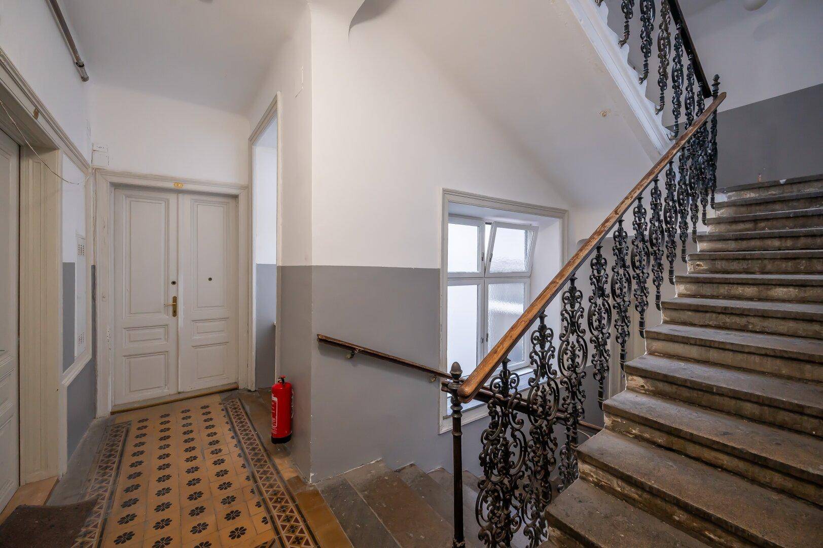 Historisches Treppenhaus mit schmiedeeisernem Geländer und gemustertem Teppich.