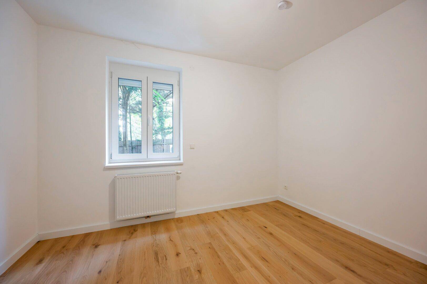 Gemütliches Schlafzimmer mit Parkettboden und Fenster zum grünen Außenbereich.