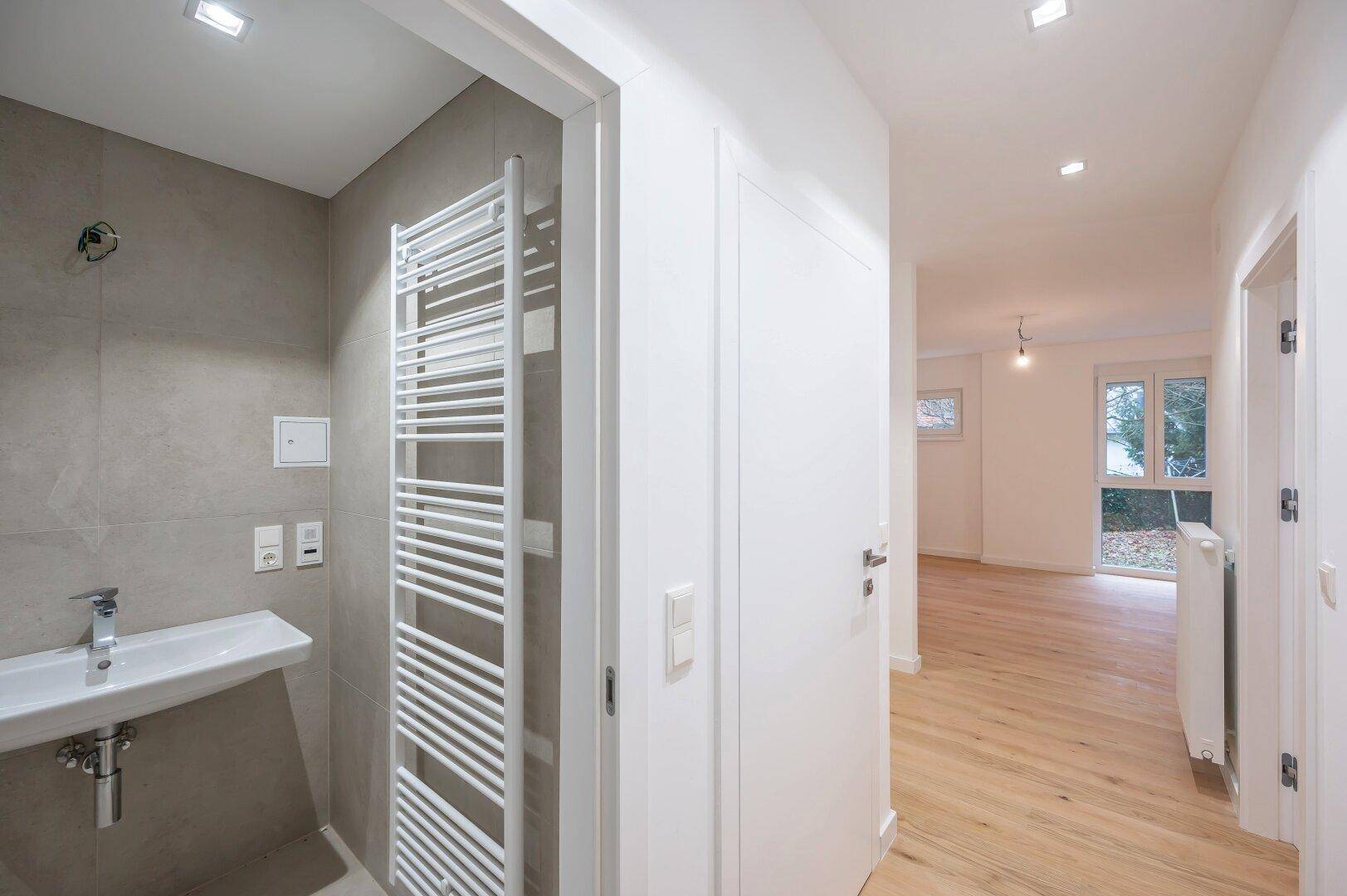 Modernes Badezimmer mit grauen Fliesen, Waschbecken und beheiztem Handtuchhalter.
