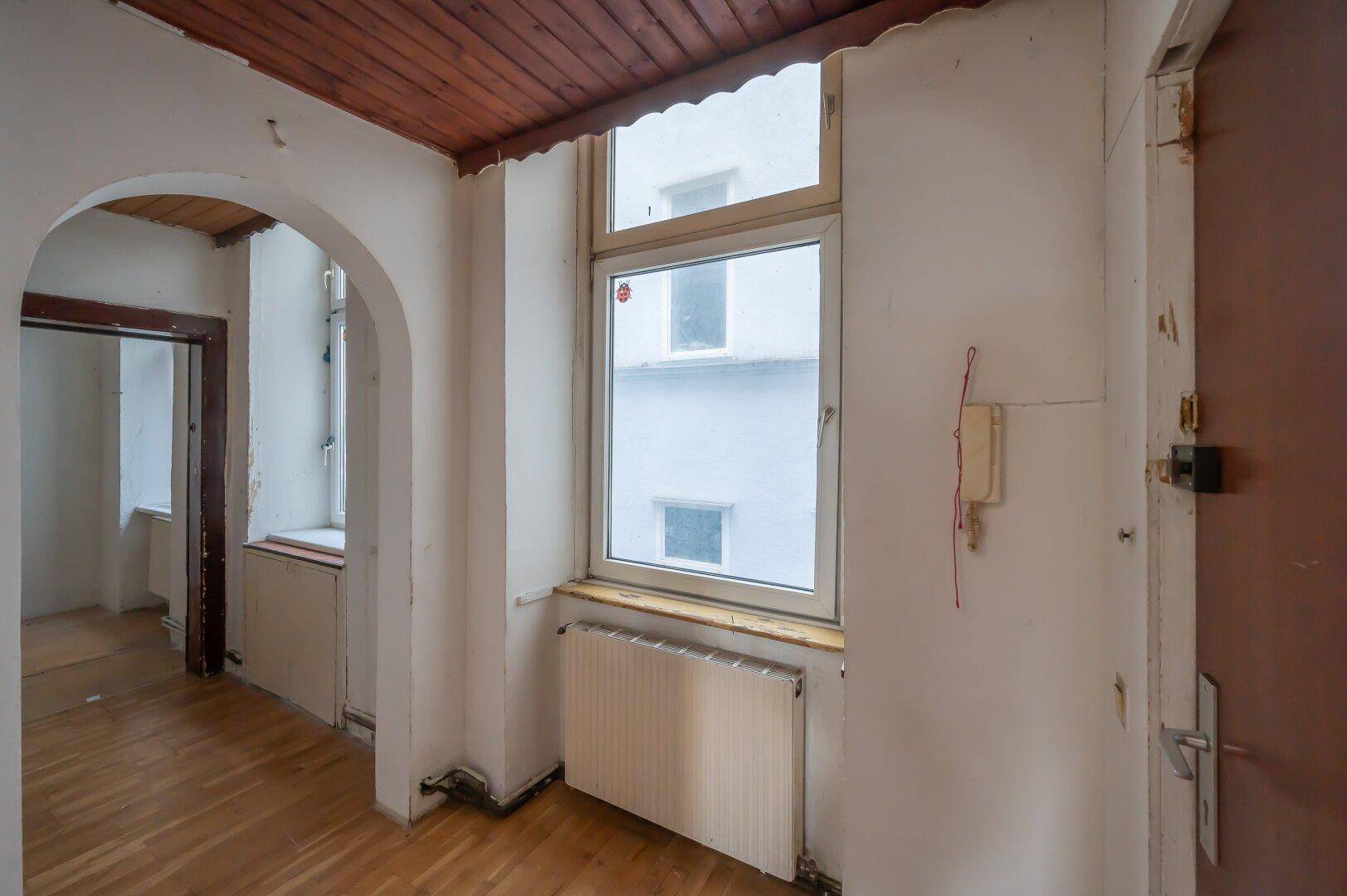 Eingangsbereich mit Holzboden, Fenster und Holztäfelung an der Decke, renovierungsbedürftig.