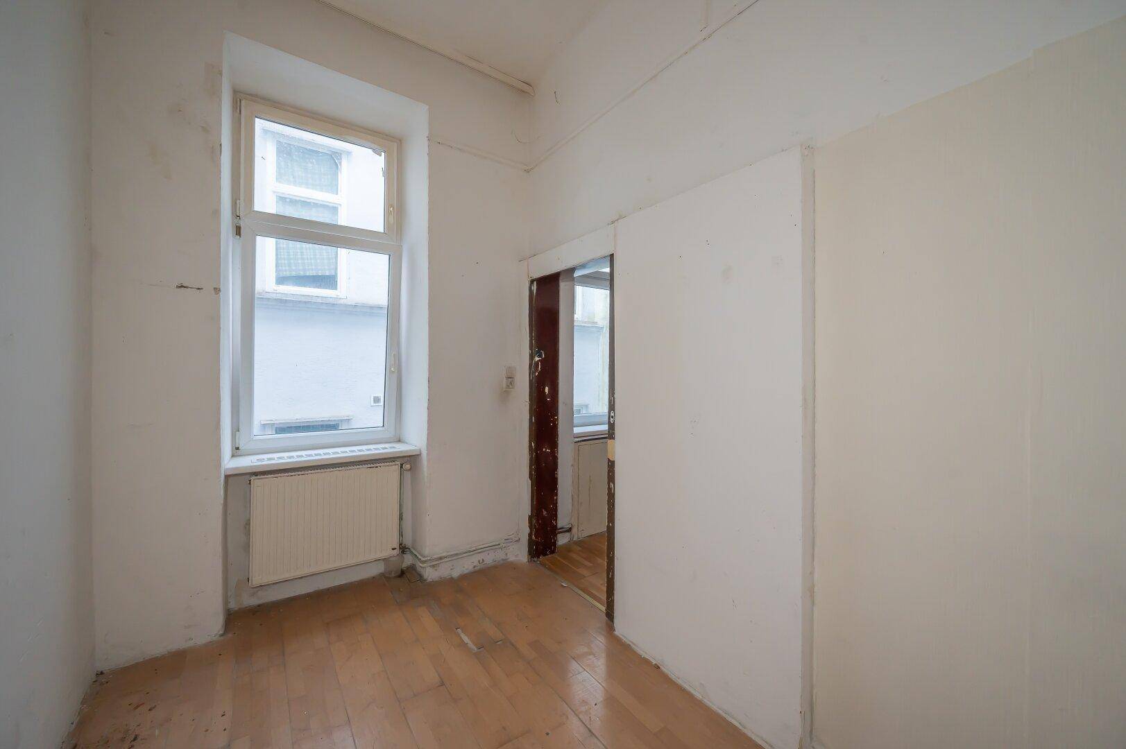 Leeres Zimmer mit Holzboden und einem Fenster, das auf eine umfassende Renovierung wartet.