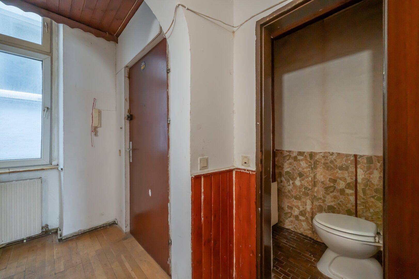 Flur mit Zugang zu einer kleinen Toilette, die eine Modernisierung benötigt.