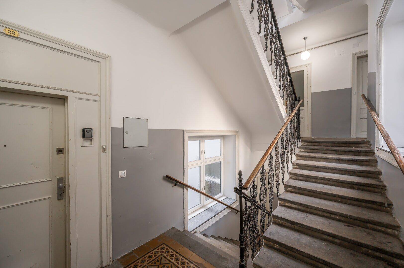 Historisches Treppenhaus mit schmiedeeisernem Geländer und Terrazzoboden im Eingangsbereich.