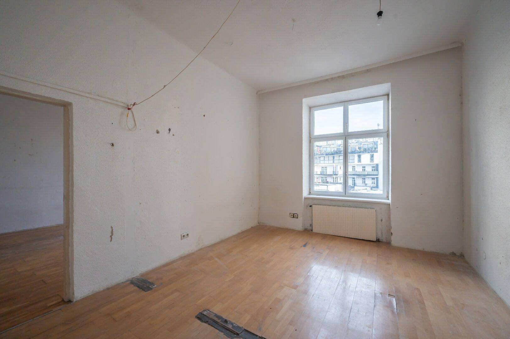 Helles, unmöbliertes Zimmer mit Holzboden und einem großen Fenster, ideal für eine Neugestaltung.