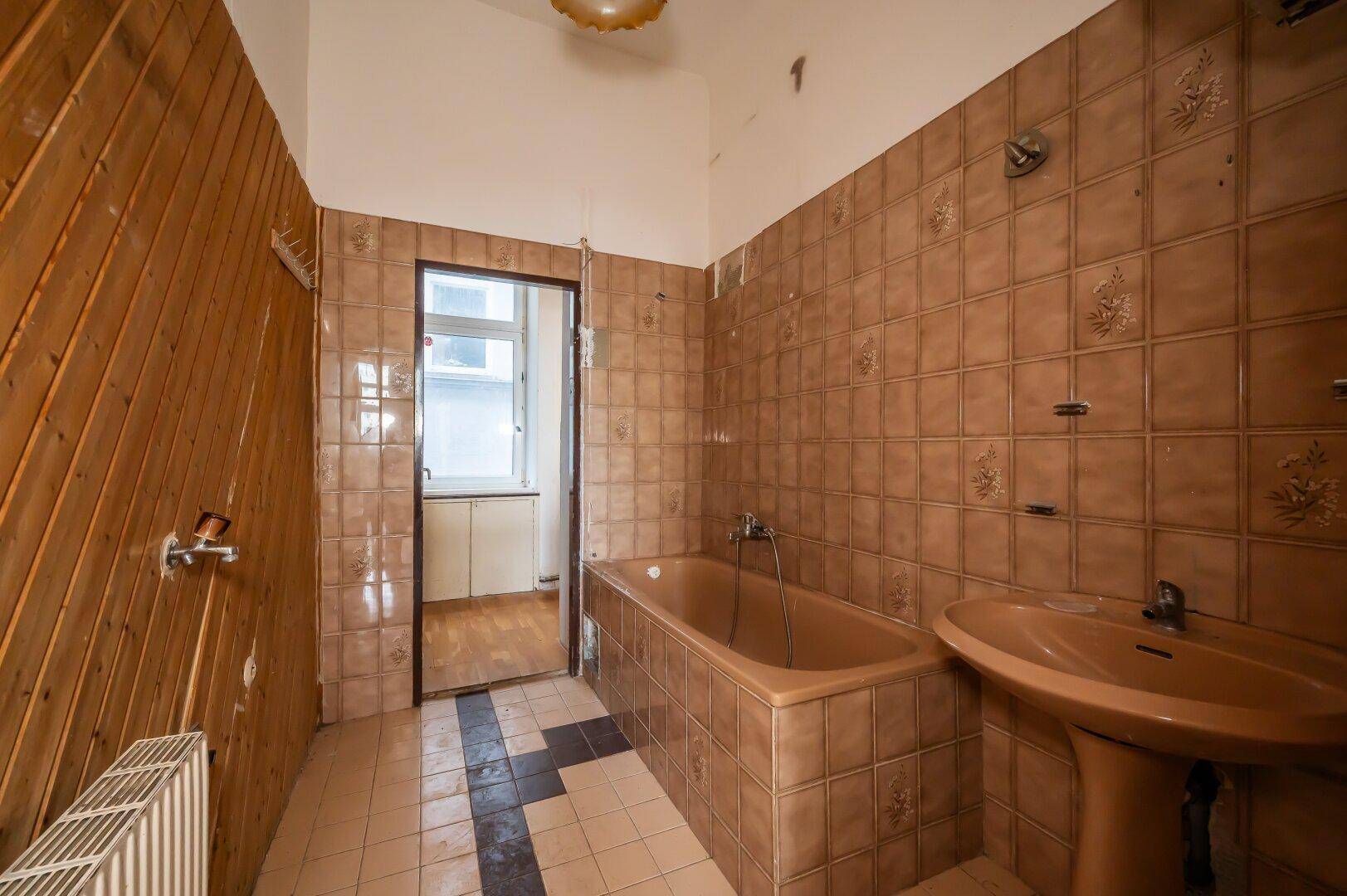 Badezimmer mit braunen Fliesen, Badewanne und Holzverkleidung, bereit für eine Renovierung.