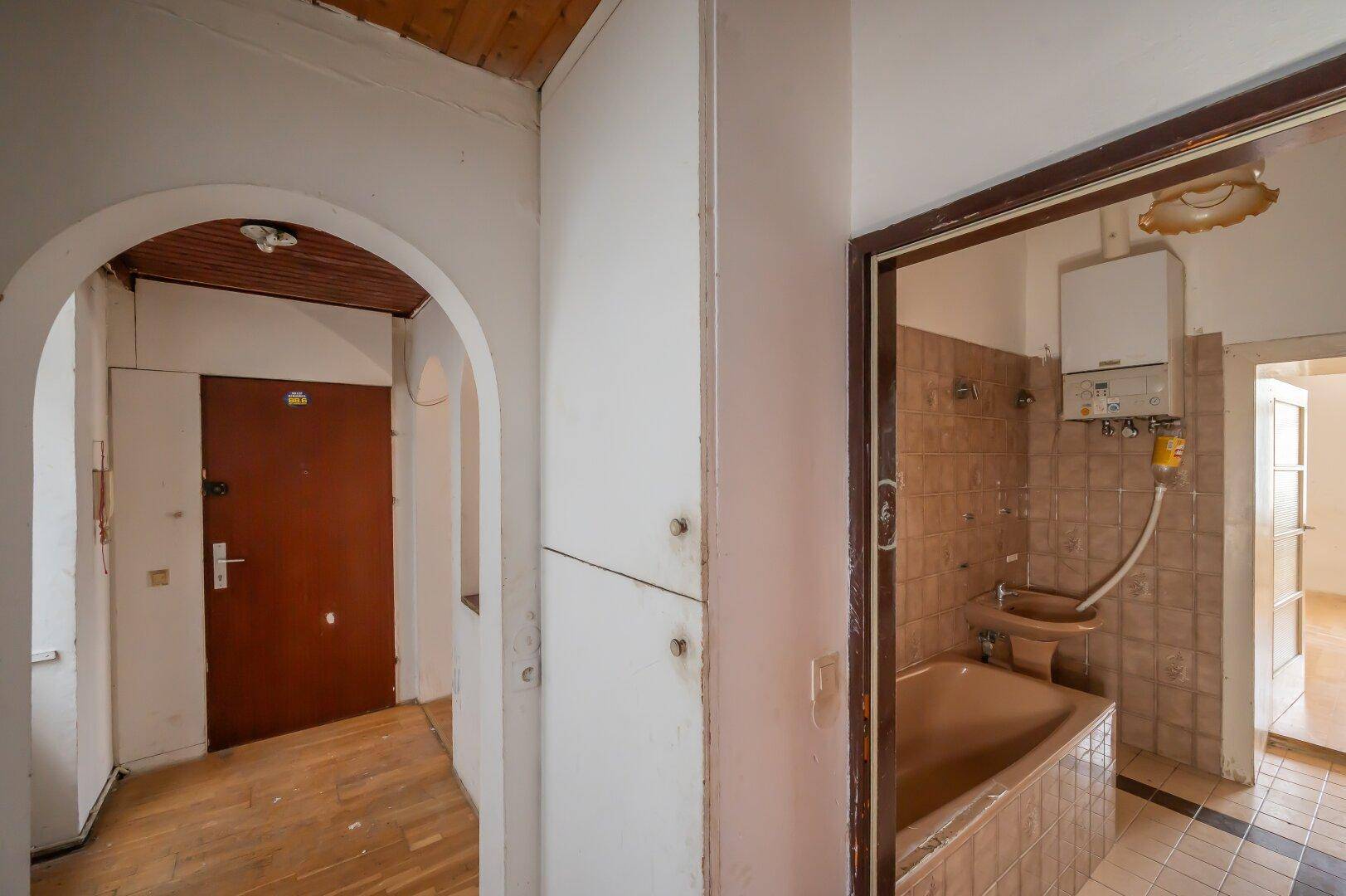 Flur mit Holzboden und Zugang zu einem Badezimmer mit Badewanne und Gastherme.