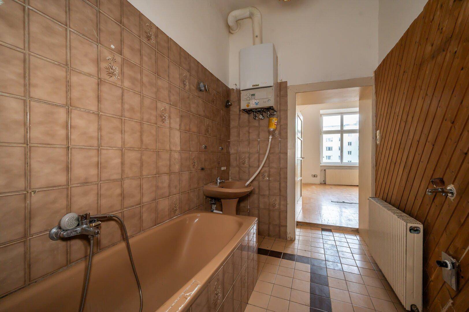 Badezimmer mit braunen Fliesen, Badewanne und Waschbecken, das eine Modernisierung benötigt.