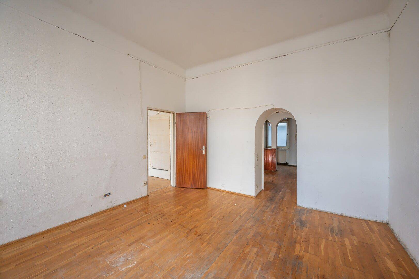 Unmöbliertes Zimmer mit Holzboden und einem Rundbogen, der zu einem weiteren Bereich führt.