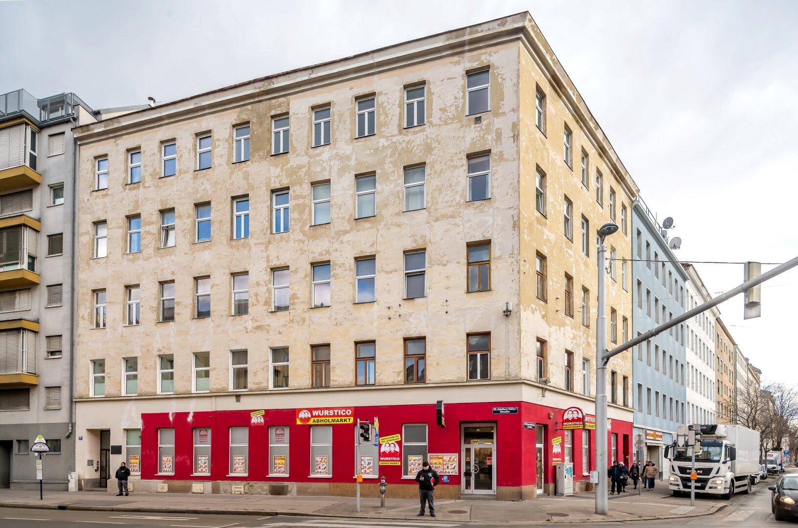 Eckgebäude mit Geschäften im Erdgeschoss und Wohnungen darüber, in einer belebten Stadtlage.