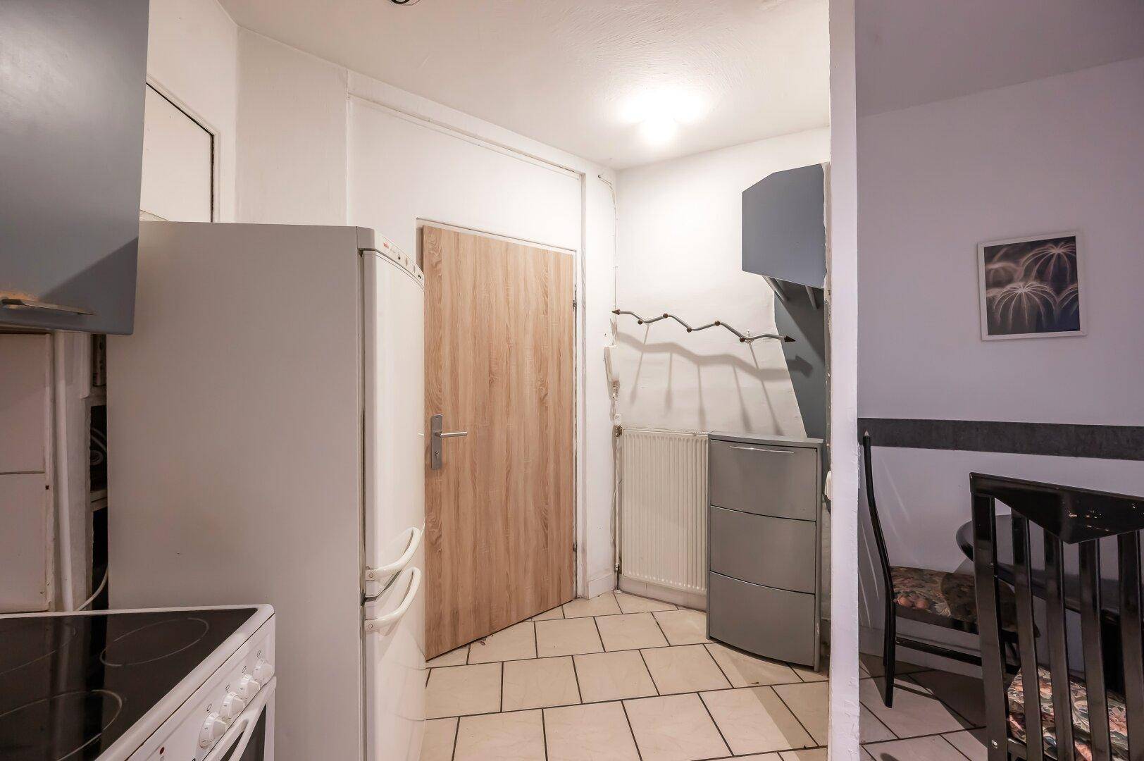 Küchenbereich mit Fliesenboden, Kühlschrank und Zugang zu einem weiteren Raum.