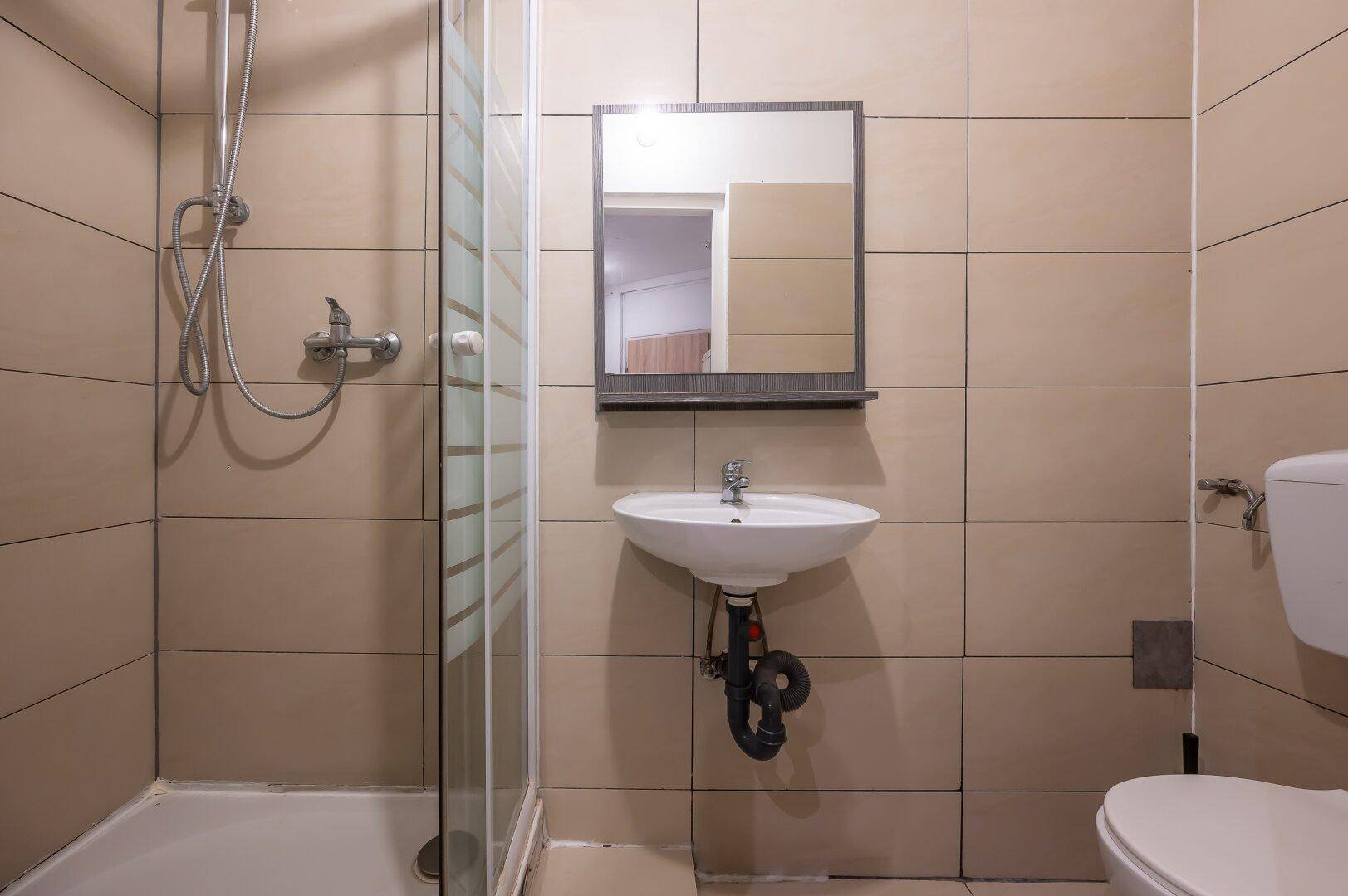 Gefliestes Badezimmer mit Duschkabine, Waschbecken und Toilette, in neutralen Farbtönen gehalten.