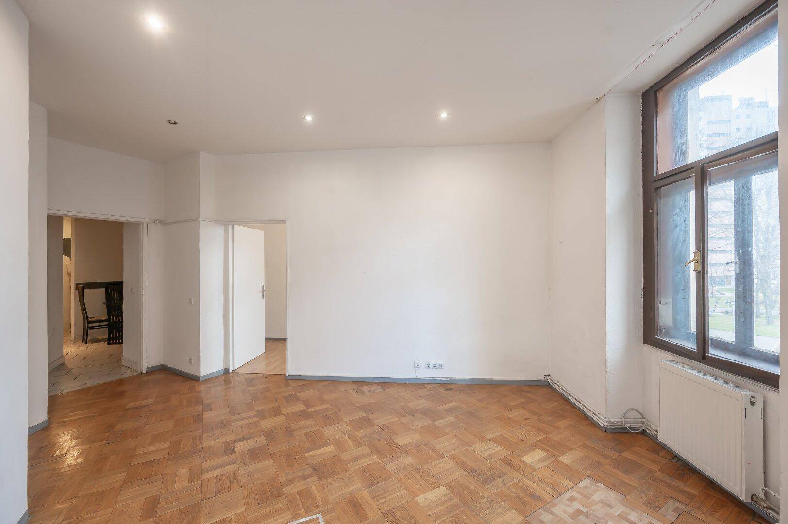 Geräumiges, leeres Zimmer mit Fischgrätparkett und großen Fenstern, ideal für eine individuelle Gestaltung.