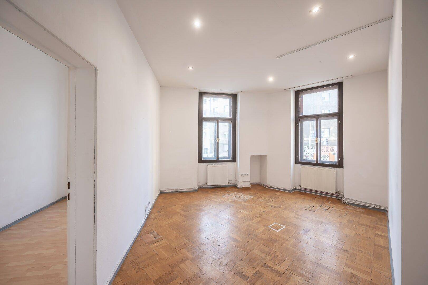 Leeres Wohnzimmer mit Fischgrätparkett, hohen Decken und großen Fenstern, bereit zur Renovierung.