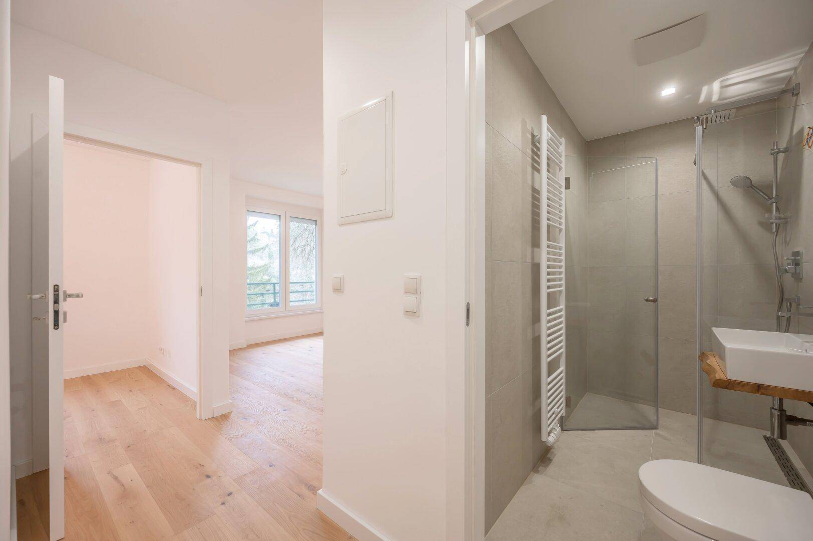Modernes Badezimmer mit Dusche und WC, angrenzend an einen hellen Raum mit Holzboden.