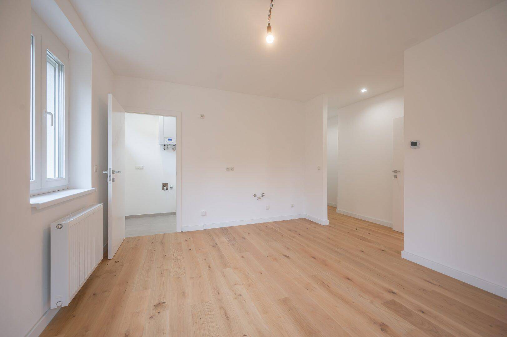 Leerer Raum mit Holzboden und Zugang zu einem Hauswirtschaftsraum mit Heizungsanlage.