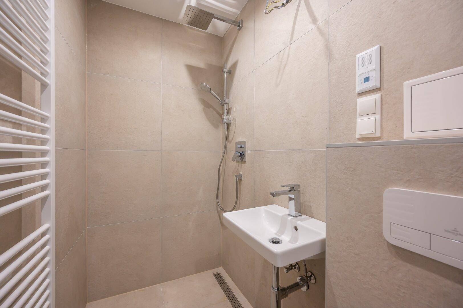Modernes Badezimmer mit beigen Fliesen, ebenerdiger Dusche und beheiztem Handtuchhalter.