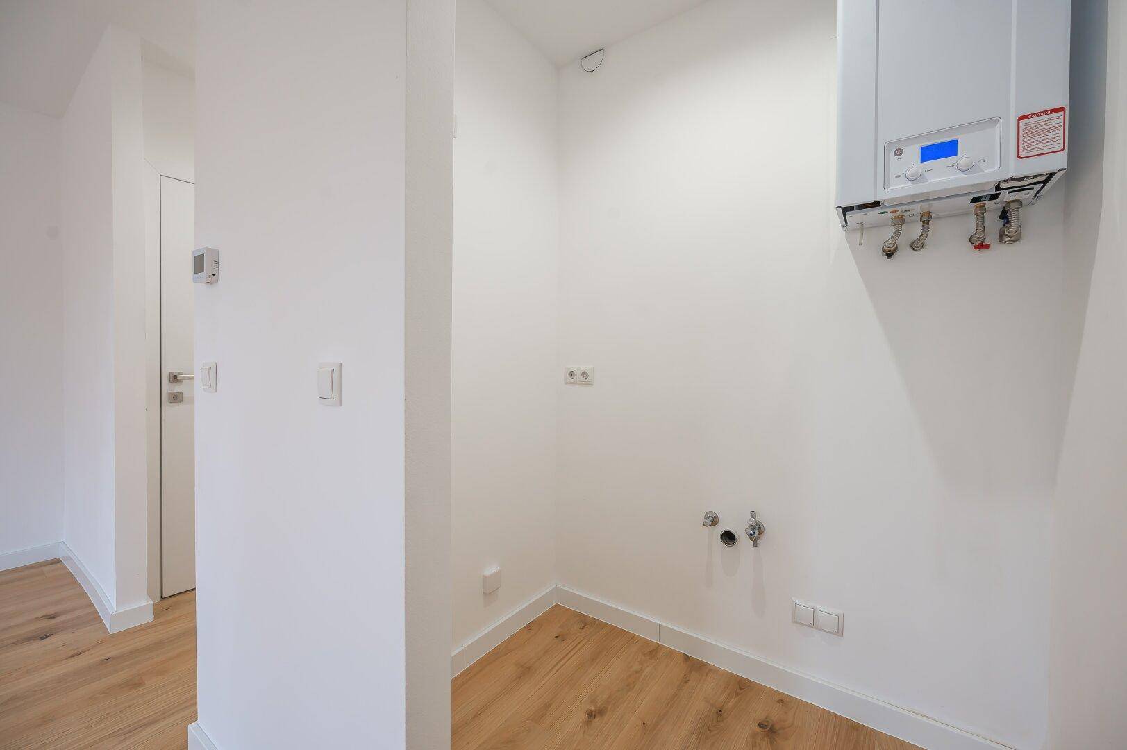 Kleiner Hauswirtschaftsraum mit Warmwasserbereiter und Anschlüssen für Waschmaschine.