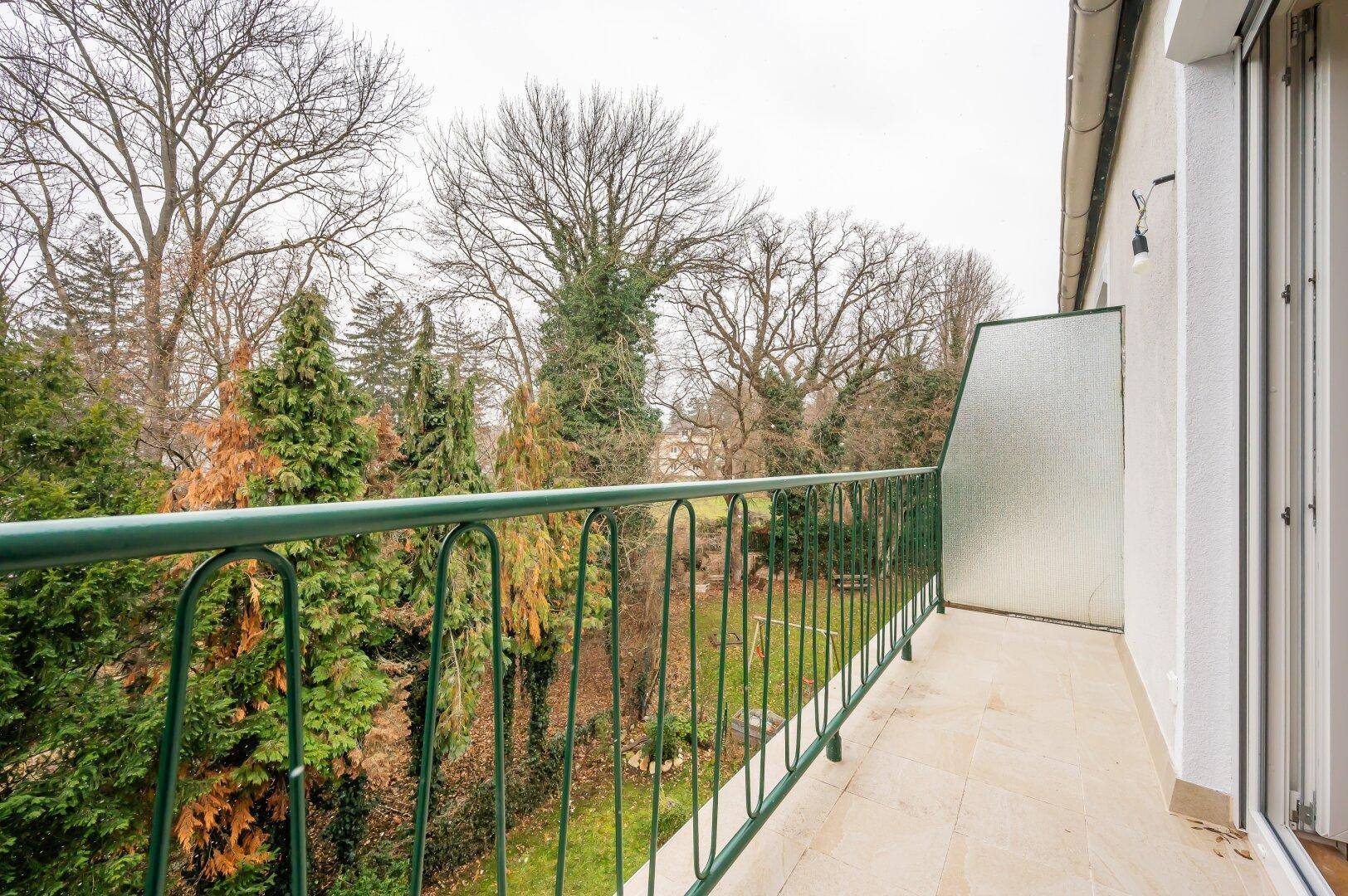 Langer Balkon mit grünem Geländer und Blick auf Bäume und Garten.