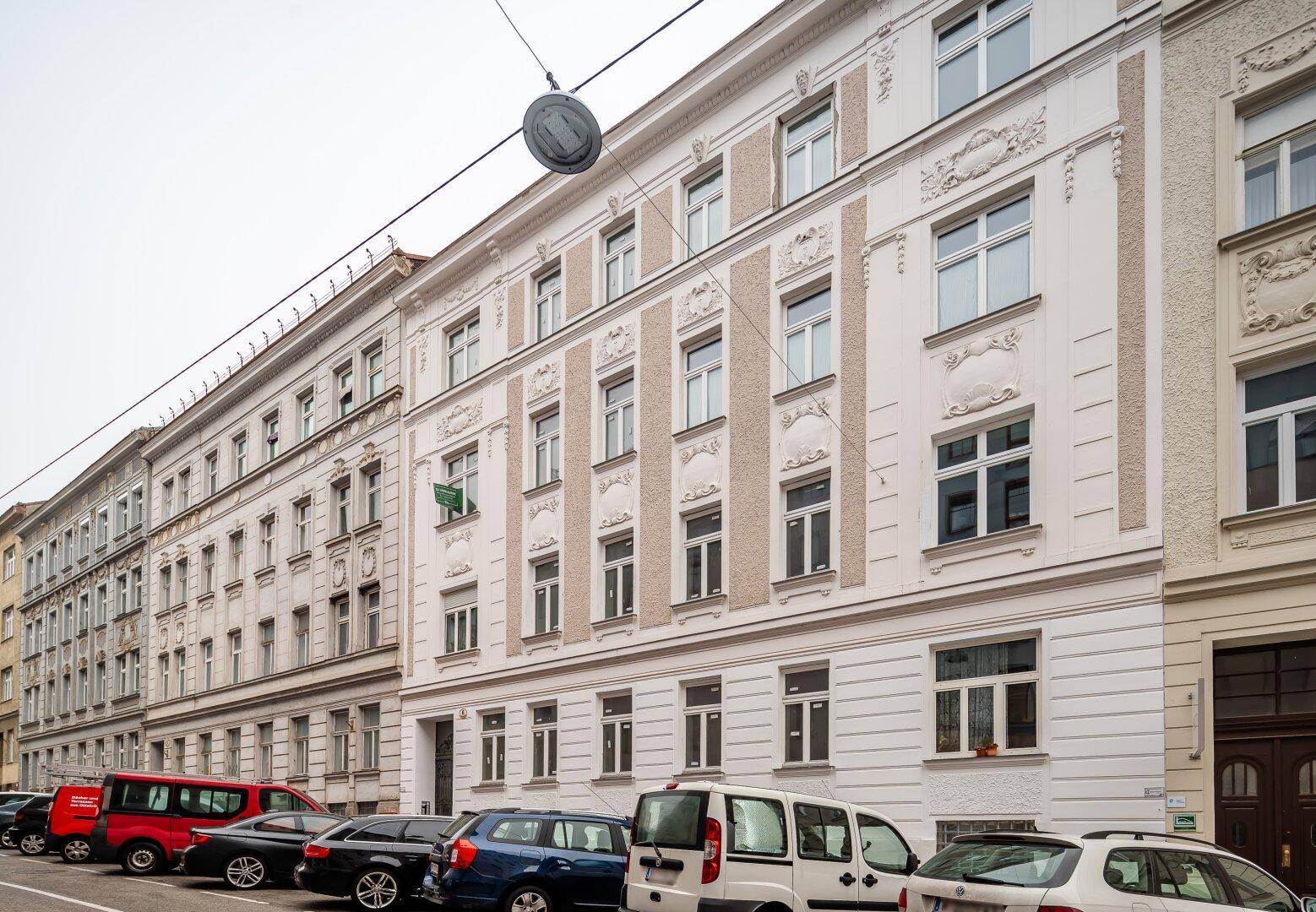 Klassische Altbaufassade mit dekorativen Elementen und parkenden Autos auf der Straße.