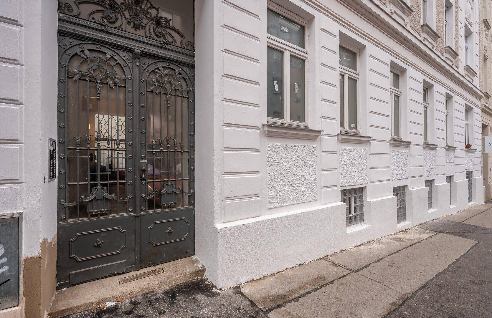 Historische Fassade mit kunstvollem Eingangstor und großen Fenstern im Erdgeschoss.