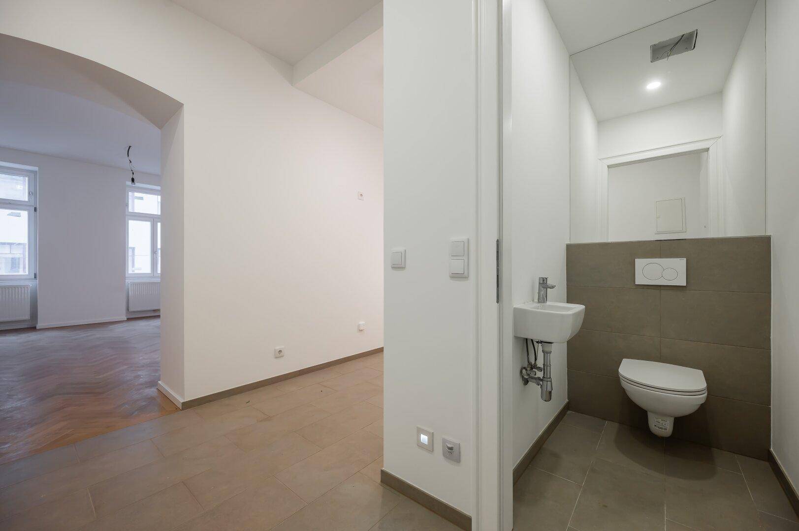 Modernes Gäste-WC mit Wand-WC, kleinem Waschbecken und Fliesenboden.