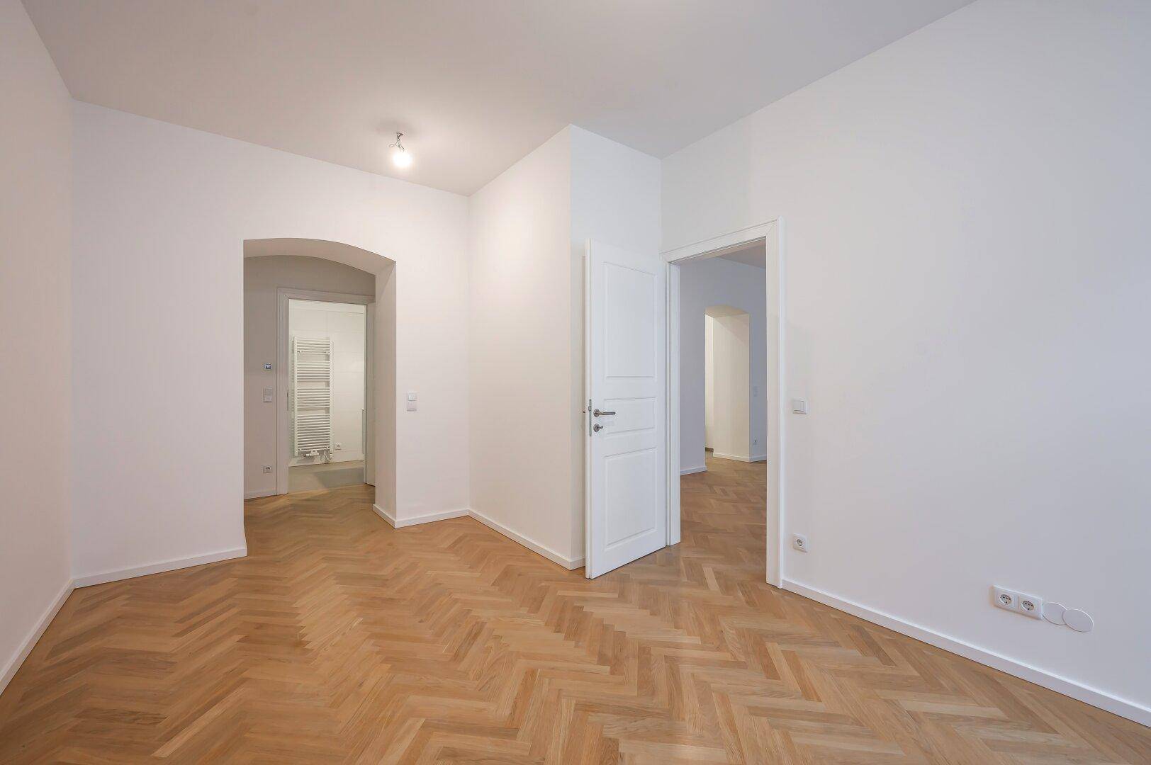 Heller Flur mit Fischgrätparkett, hohen Decken und Zugang zu verschiedenen Räumen.