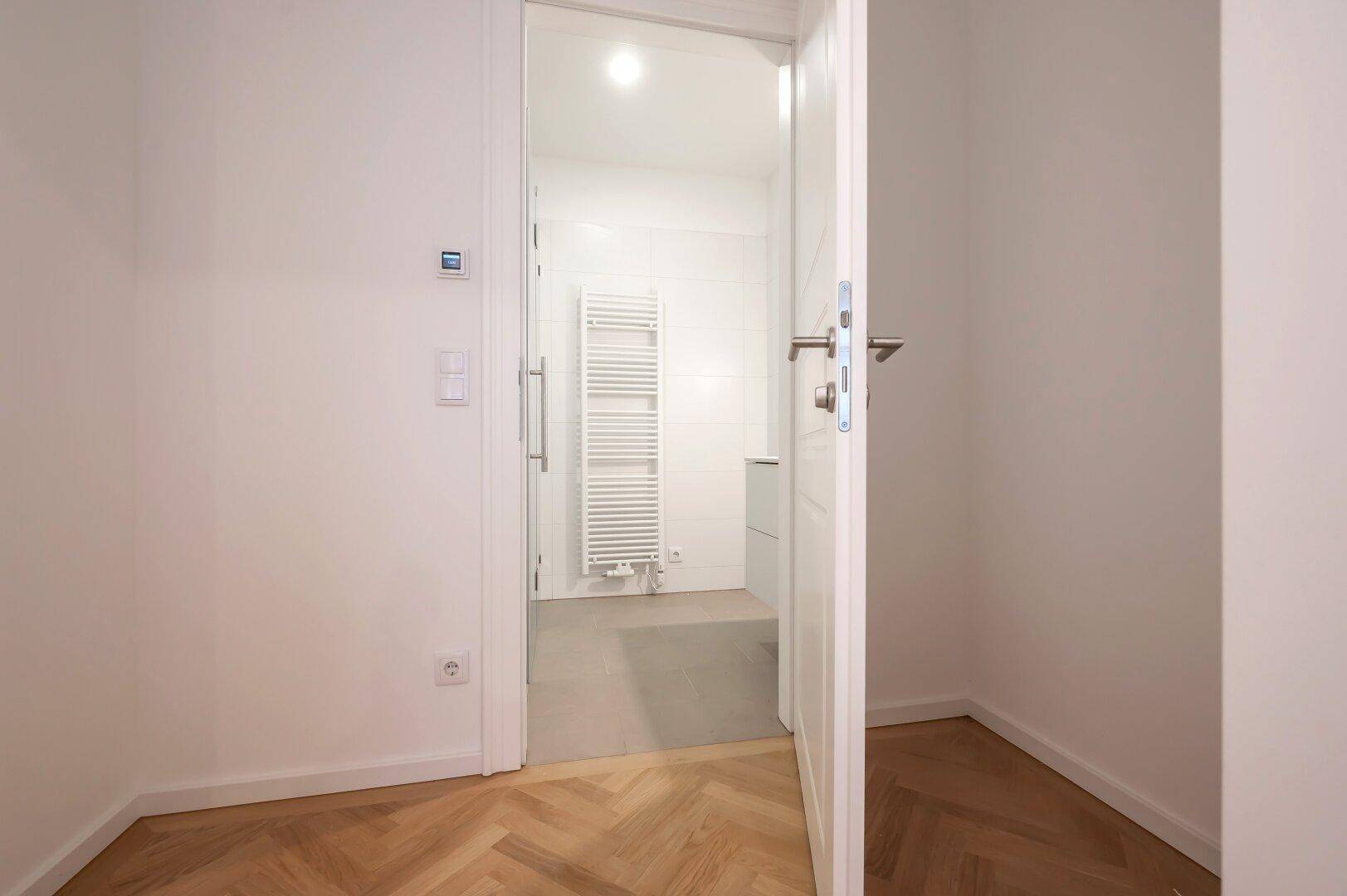 Blick in ein modernes Badezimmer mit Handtuchheizkörper und Duschbereich.