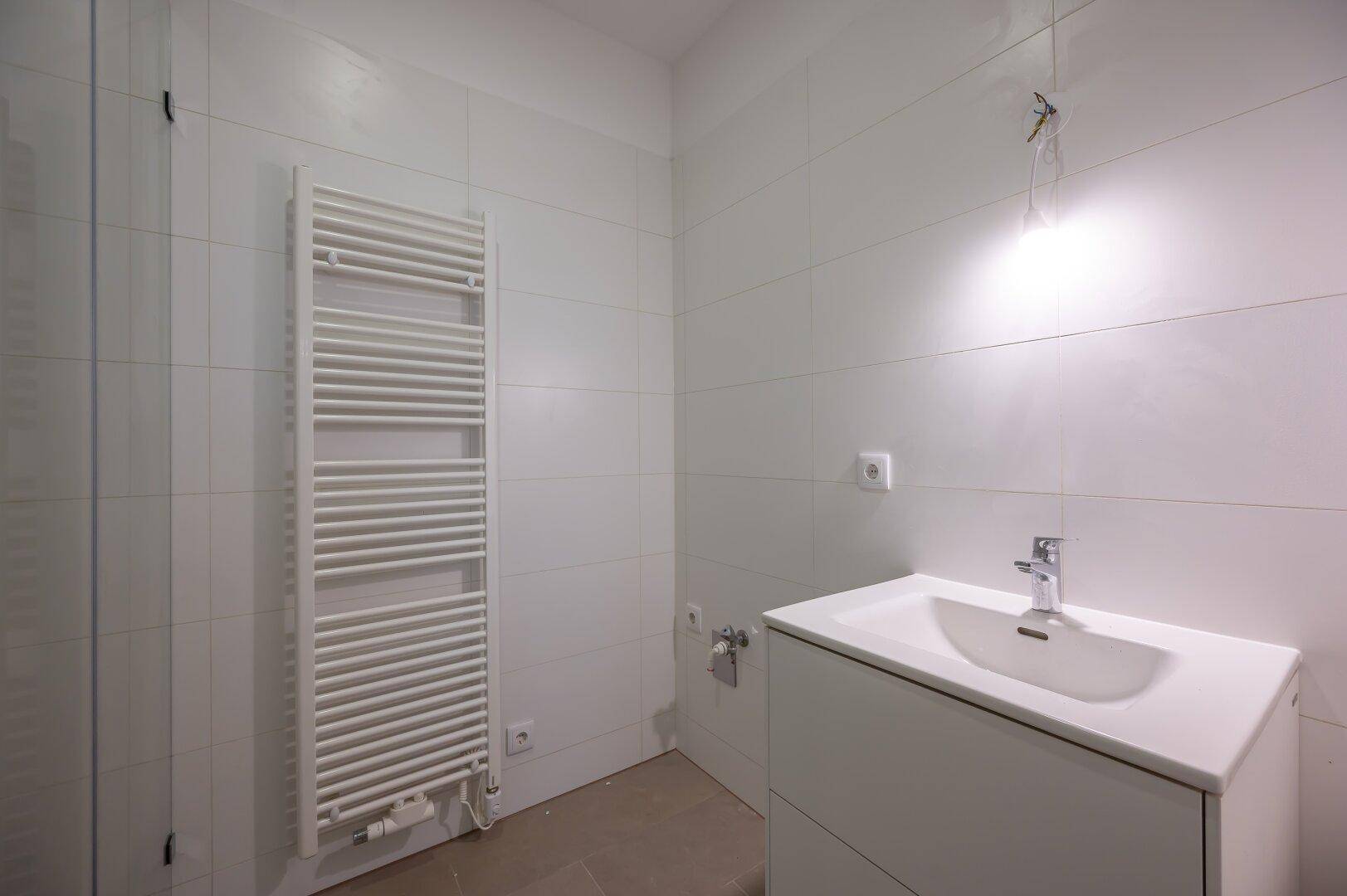 Modernes Badezimmer mit Waschtischunterschrank, Handtuchheizkörper und weißen Fliesen.