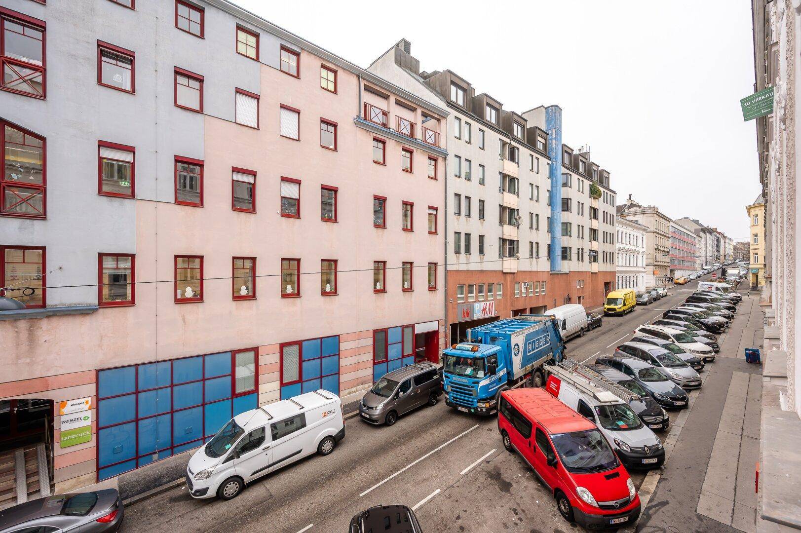 Straßenansicht eines Wohngebäudes mit parkenden Autos und städtischer Umgebung.