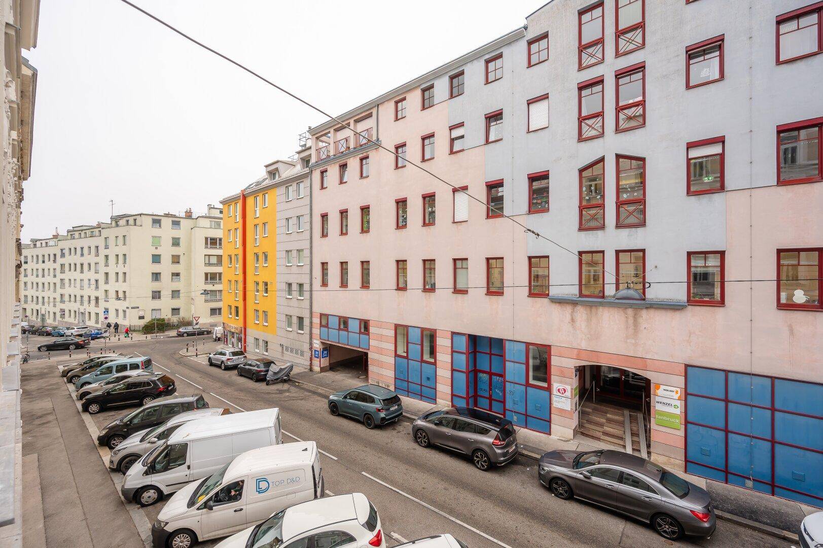 Straßenansicht eines Wohngebäudes mit parkenden Autos und umliegender Bebauung.