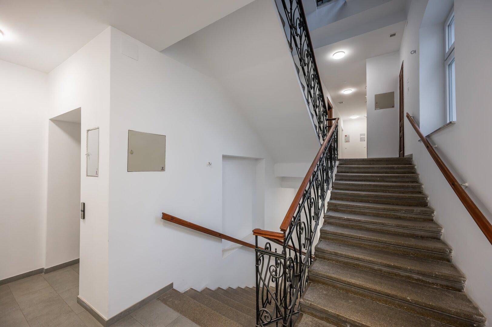 Elegantes Treppenhaus mit schmiedeeisernem Geländer und Holzhandlauf in einem Altbau.