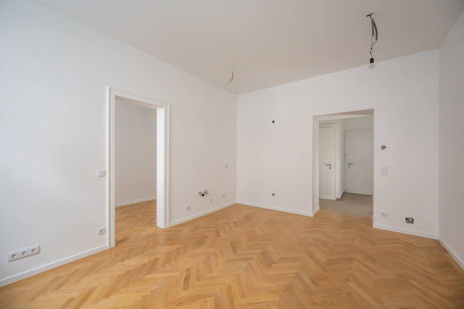 Geräumiges Zimmer mit Fischgrätparkett und mehreren Türöffnungen, ideal für offene Wohnkonzepte.