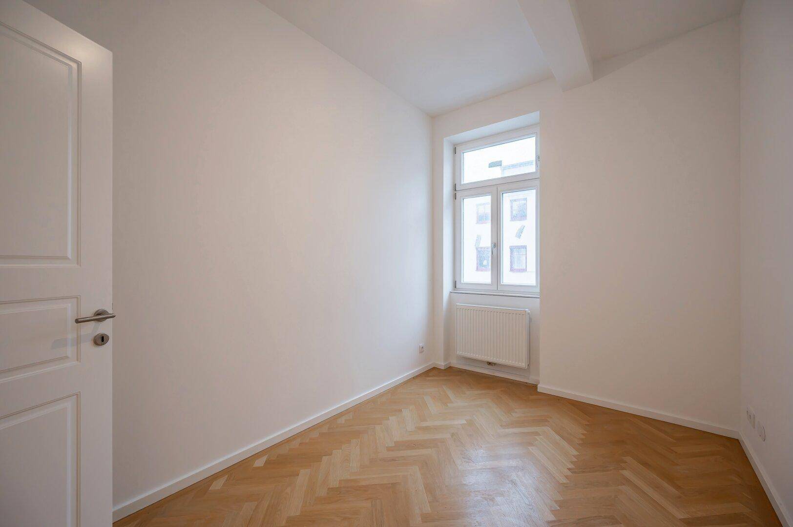 Ruhiges Zimmer mit Fischgrätparkett und Fenster, ideal als Schlaf- oder Arbeitszimmer.