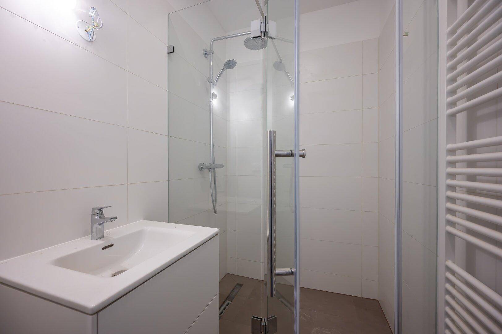 Modernes Duschbad mit Glasduschkabine, Waschtisch und beheiztem Handtuchhalter.