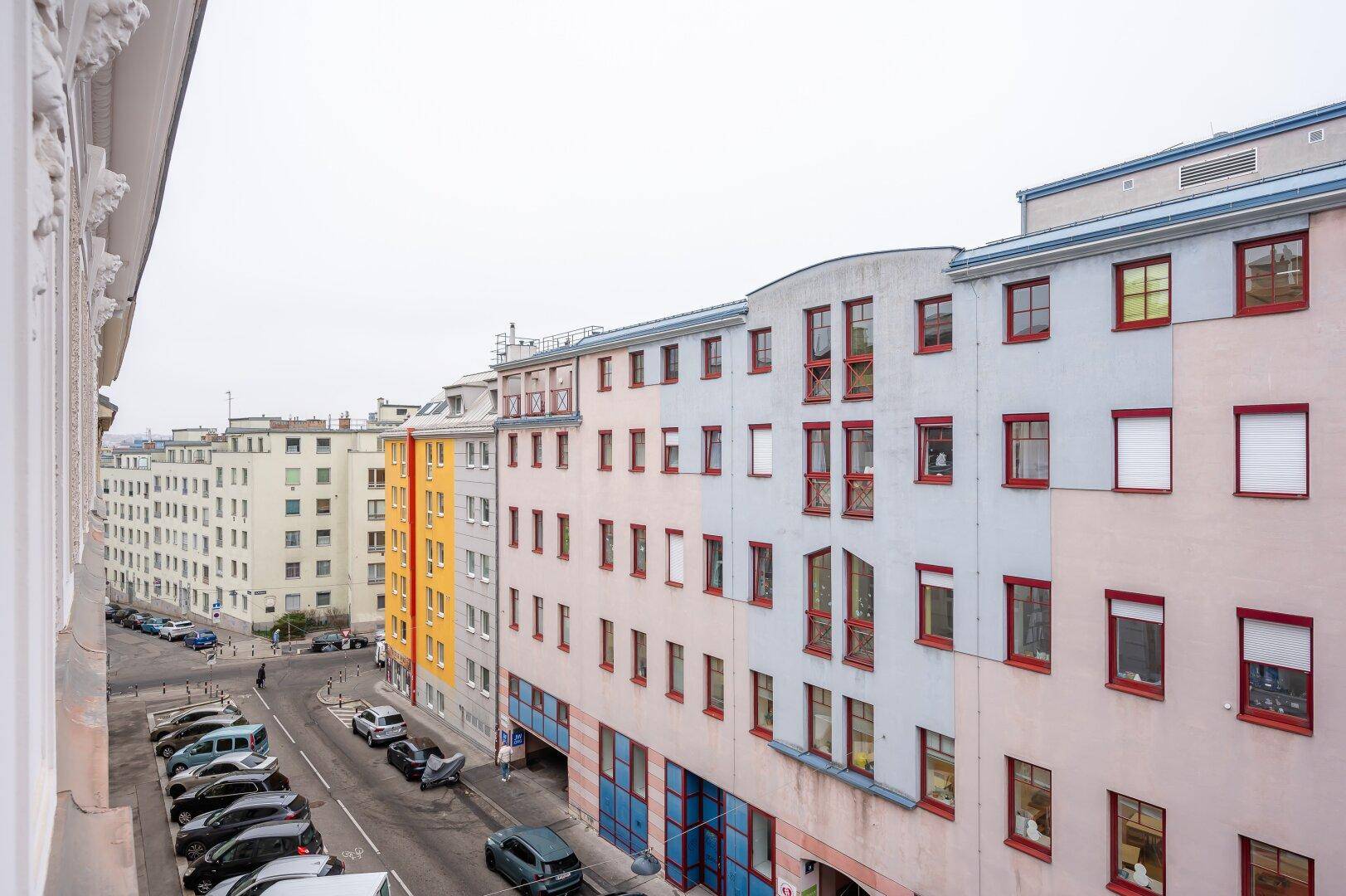 Blick auf eine belebte Straße mit verschiedenen Wohngebäuden und parkenden Autos.