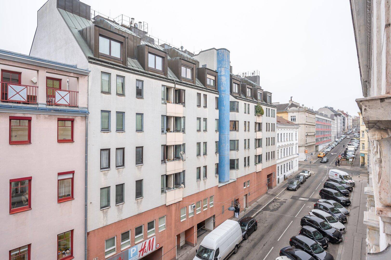 Weitläufiger Blick auf eine Stadtstraße mit parkenden Fahrzeugen und Wohngebäuden.