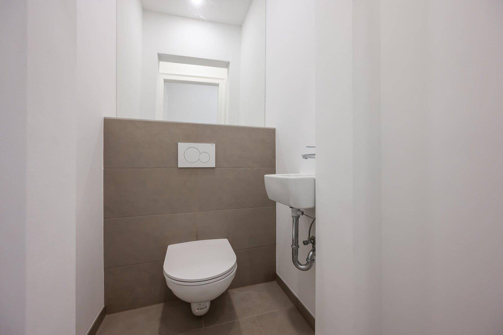 Funktionales Gäste-WC mit Wand-WC, kleinem Waschbecken und modernen Fliesen.