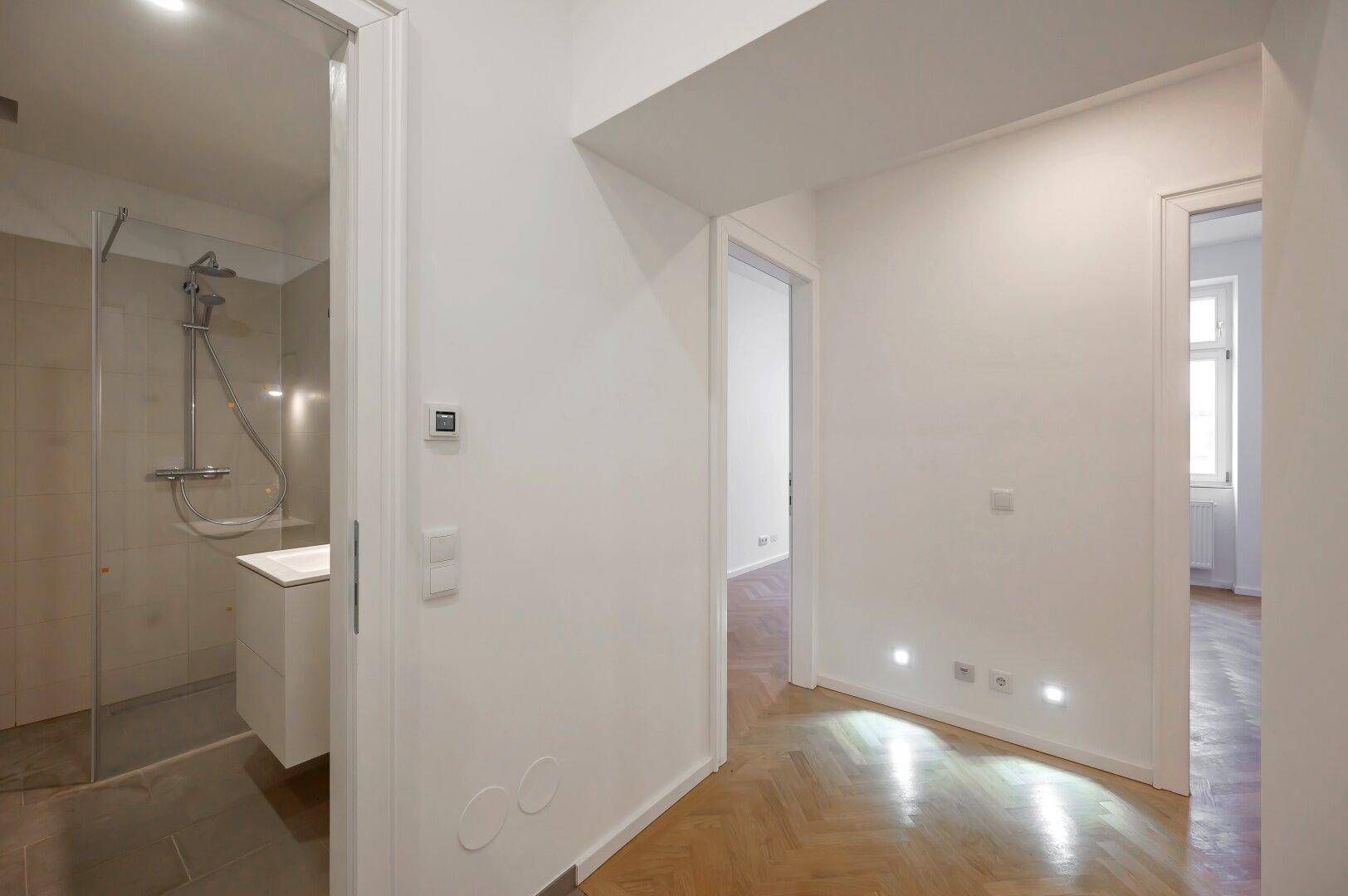 Heller Flur mit integrierten Bodenleuchten und Blick in ein modernes Duschbad.